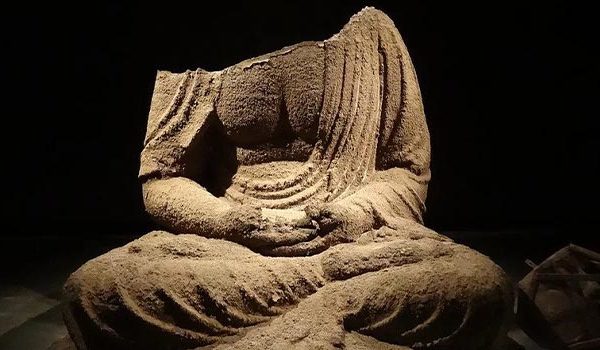 Headless Buddah statue surrounded by ashes