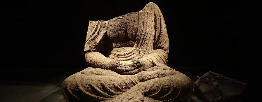 Headless Buddah statue surrounded by ashes